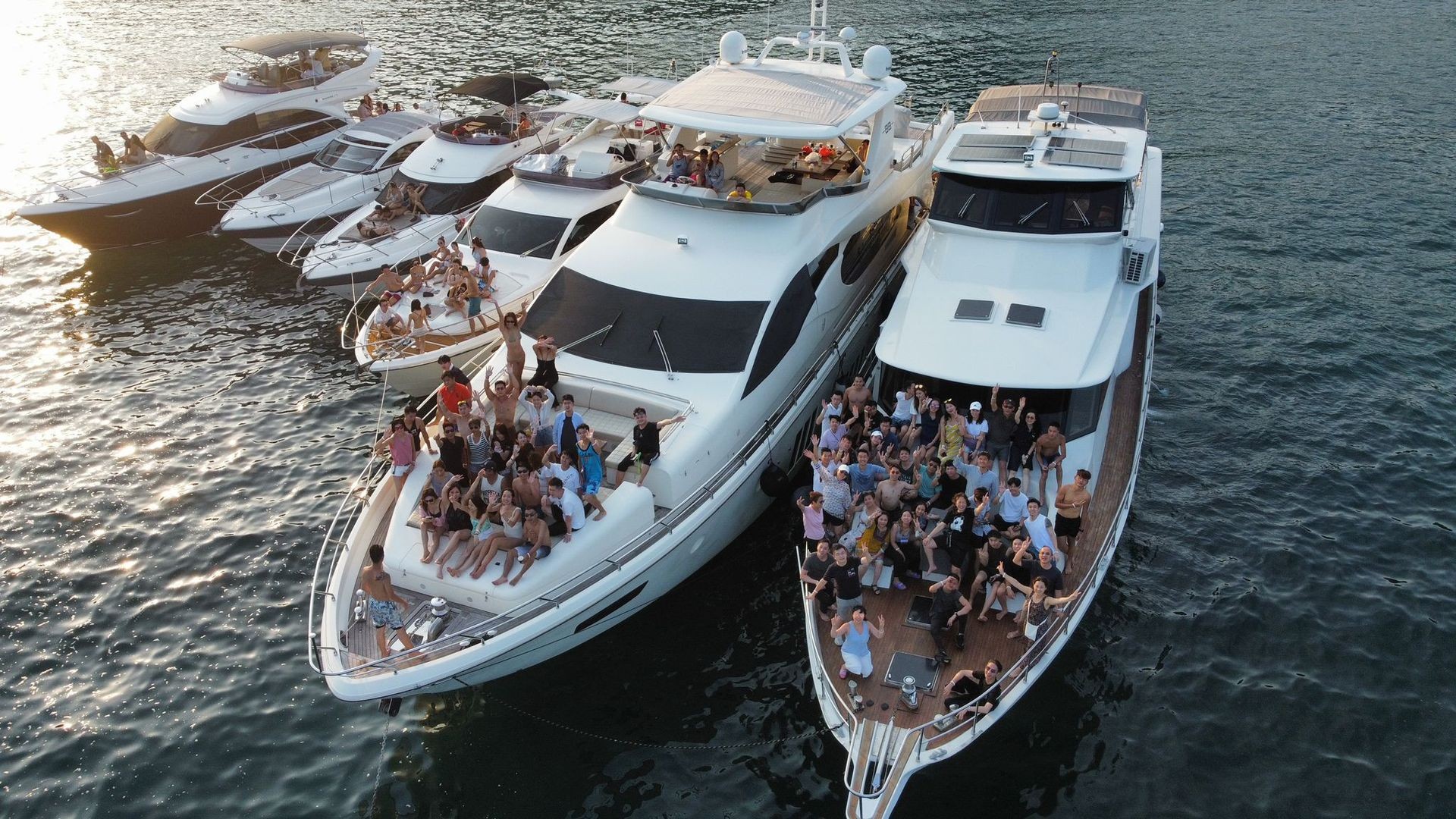 Large group of people partying and socializing on multiple yachts tied together on the water.